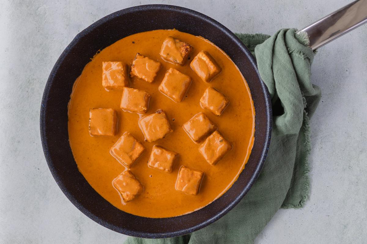 paneer chucks simmering in skillet with sauce.