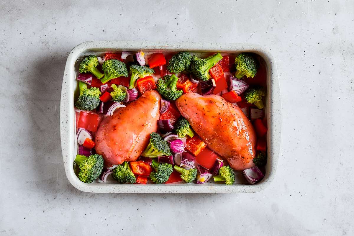 vegetables and raw chicken breasts on a sheet pan.