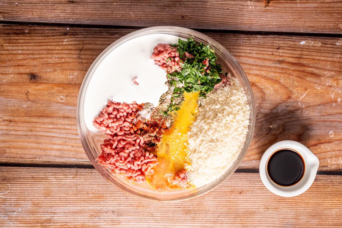 ground beef, eggs, bread crumbs, herbs, and cream in a bowl.