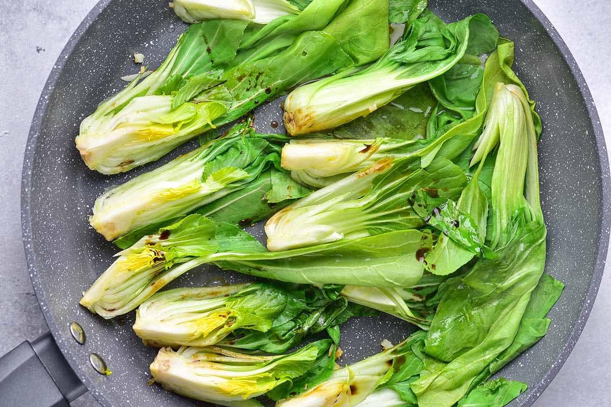 seasonings added to bok choy in a skillet.