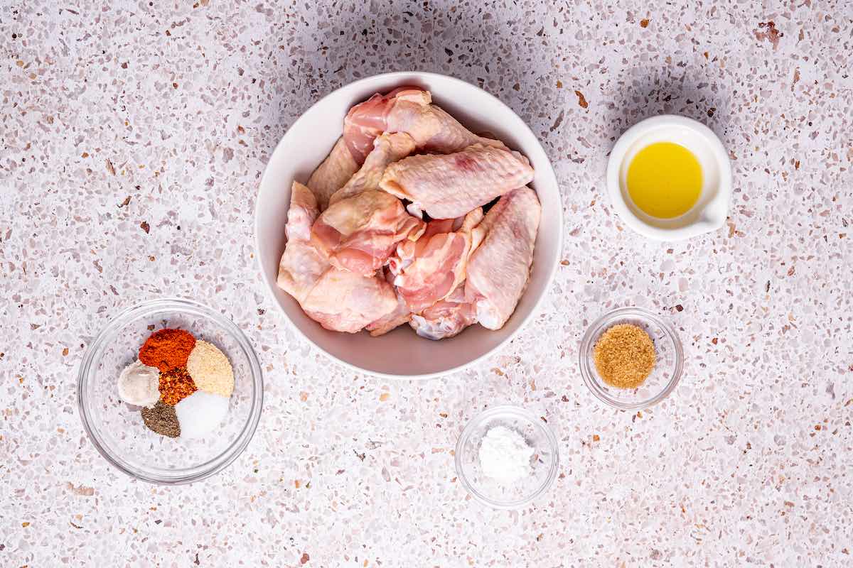 raw chicken wings in a bowl with seasonings in other bowls.