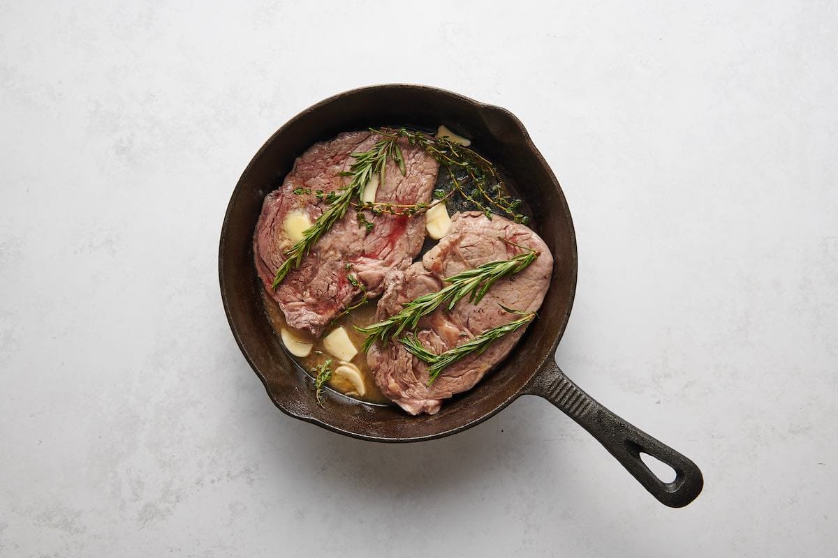 ribeye steaks simmering with garlic butter and herbs.