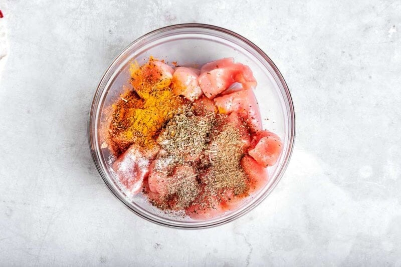 raw chicken with seasonings in a mixing bowl.