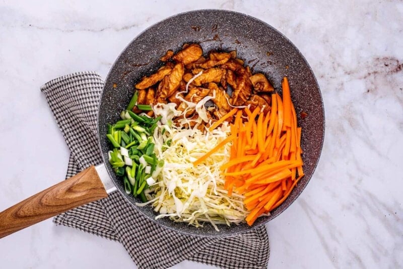 adding vegetables to the skillet with the chicken.