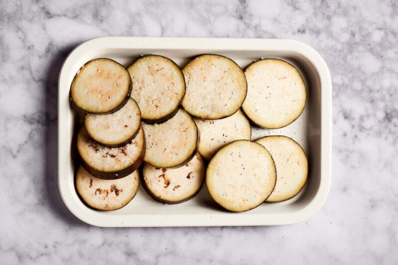 raw eggplant rounds in a baking dish.