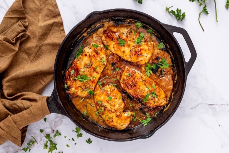 honey mustard chicken in a skillet with fresh herbs on top.