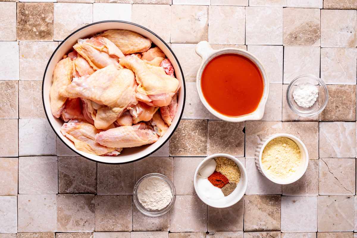 raw chicken wings in a bowl, along with buffalo sauce and seasonings.