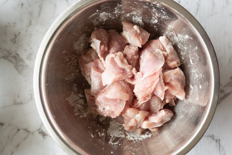 raw chopped chicken thighs with flour in a bowl.