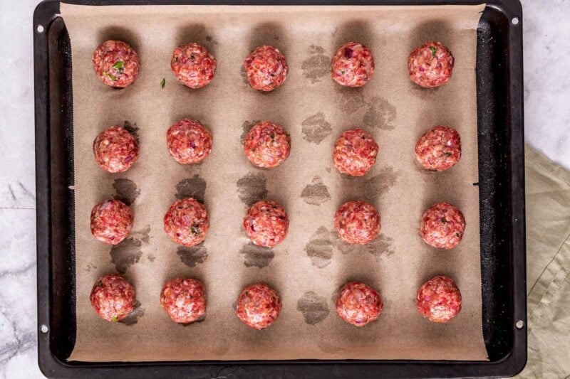 raw shaped meatballs on a baking sheet.