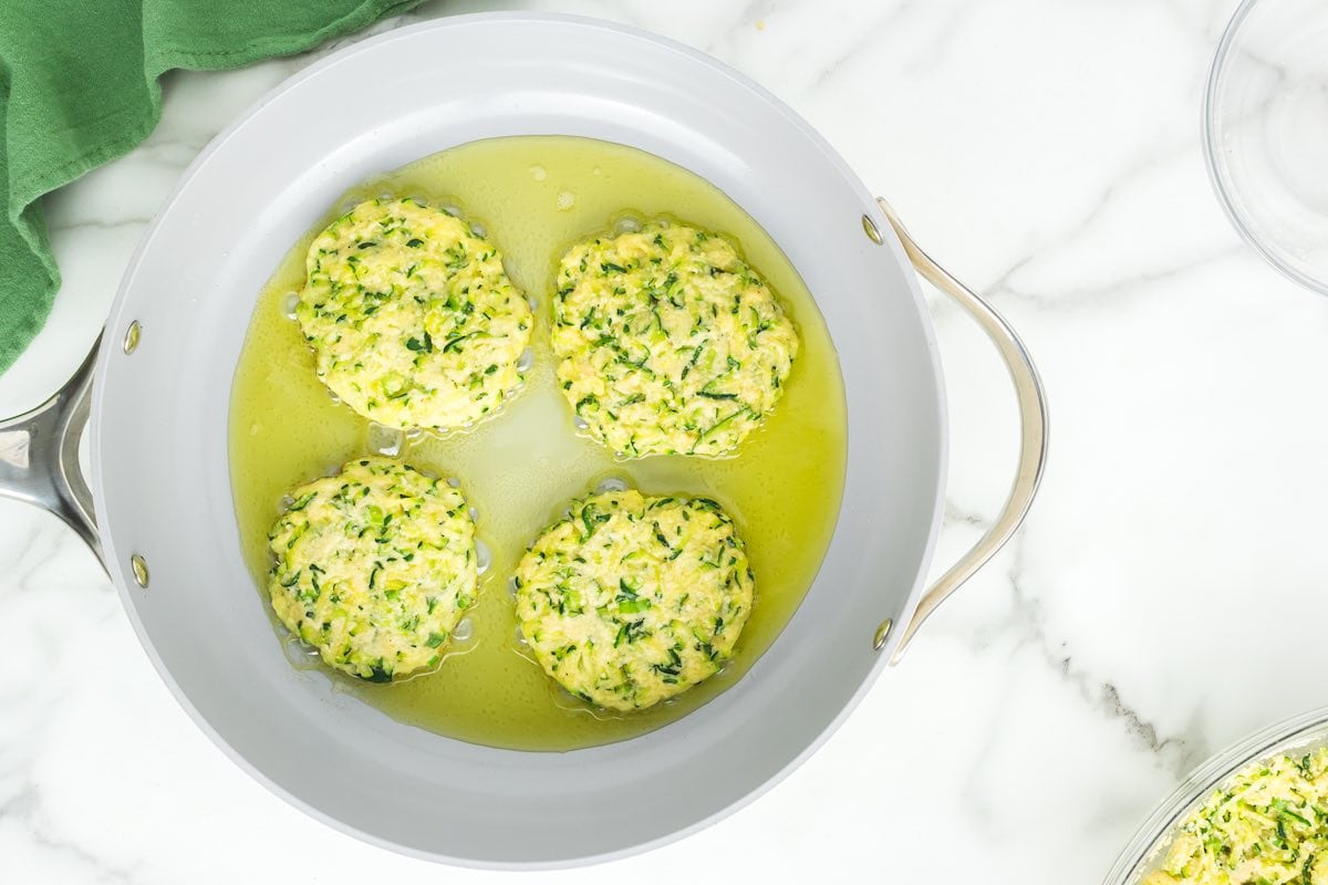 zucchini fritters frying in a skillet.