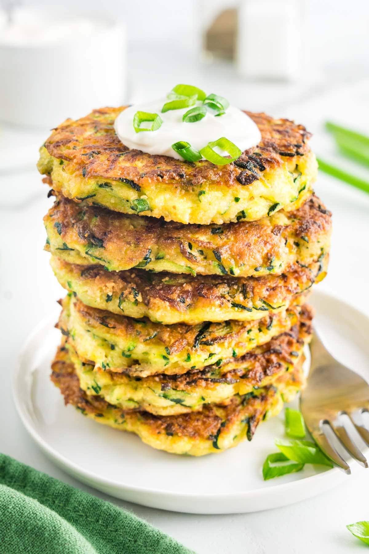 stack of zucchini fritters with sour cream on top.