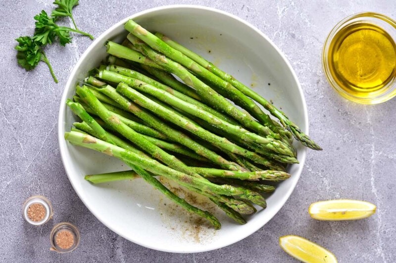 seasoned and raw asparagus in a bowl.