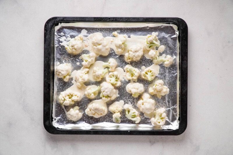 raw battered cauliflower on a baking sheet.