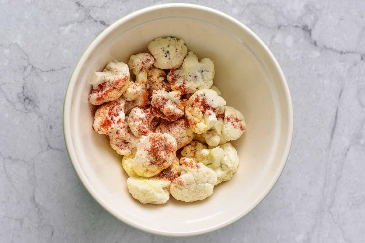 raw cauliflower florets in a bowl with seasonings.