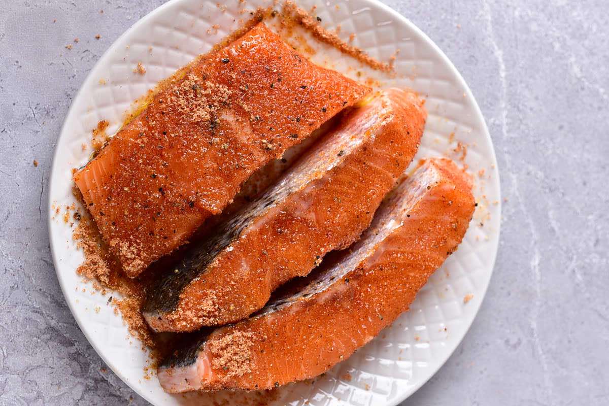 raw salmon fillets mixed with seasonings on a plate.