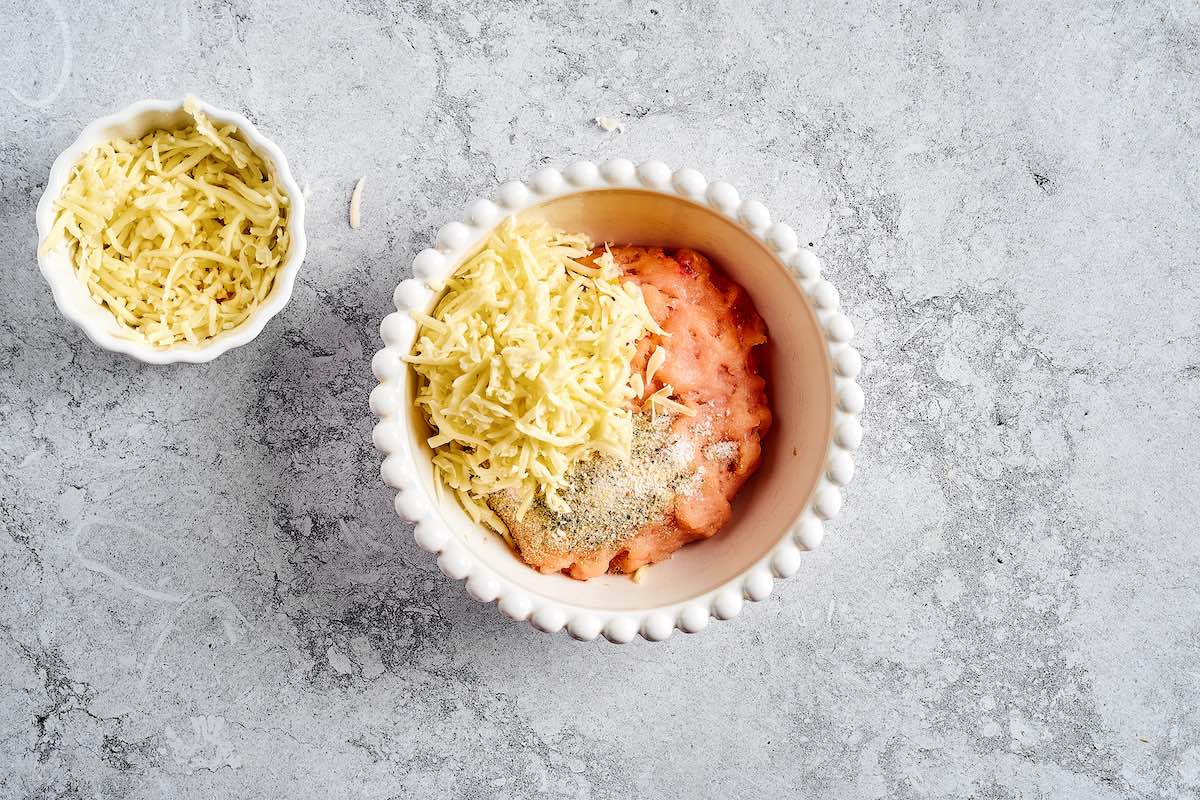 raw ground chicken, shredded cheese, and seasonings in a bowl.