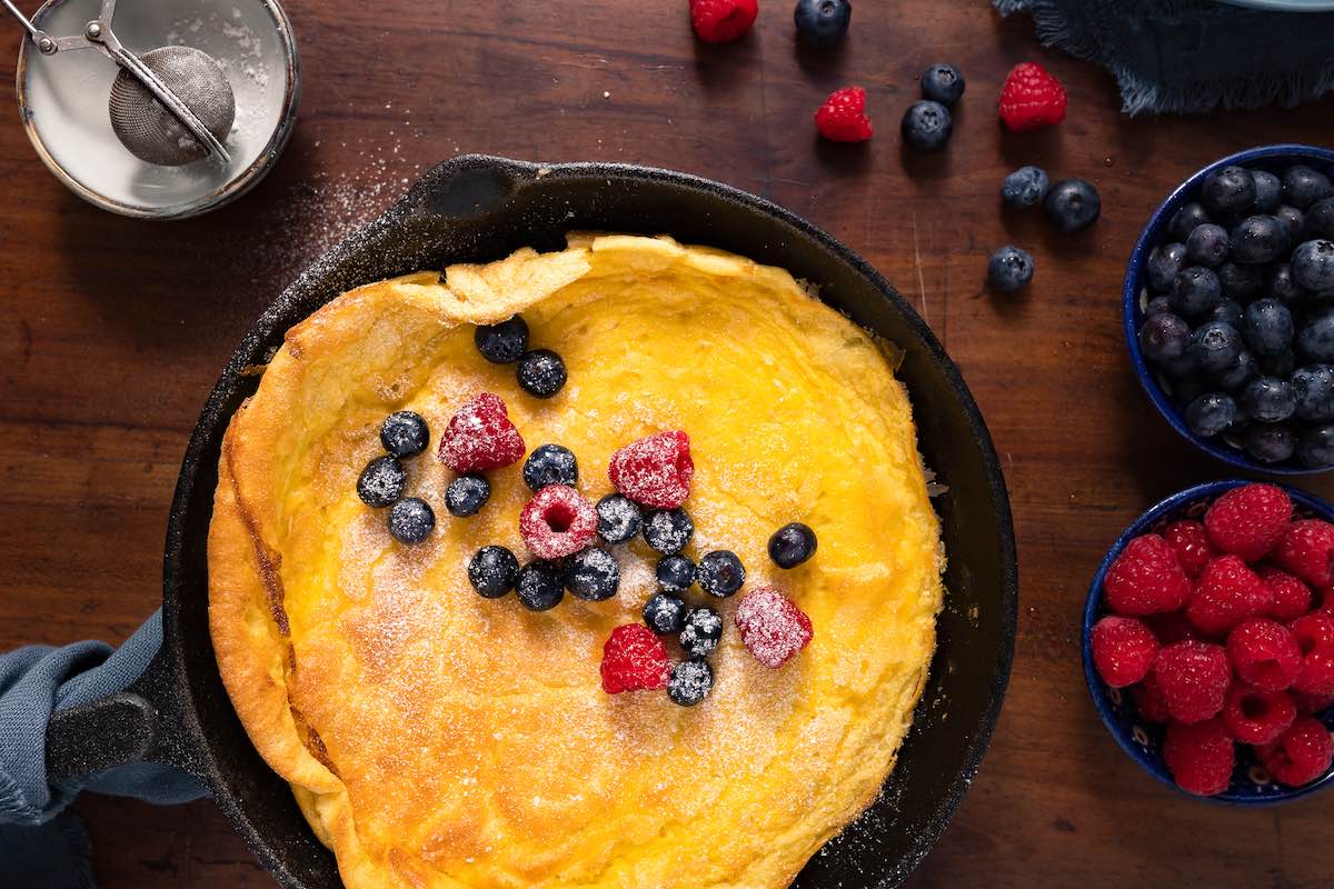 skillet pancake with powdered sugar and berries on top.