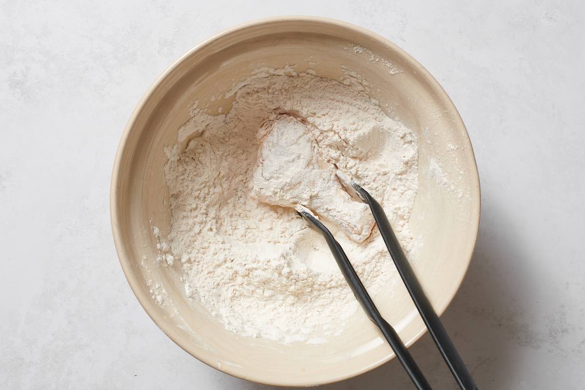 dipping raw chicken in flour.