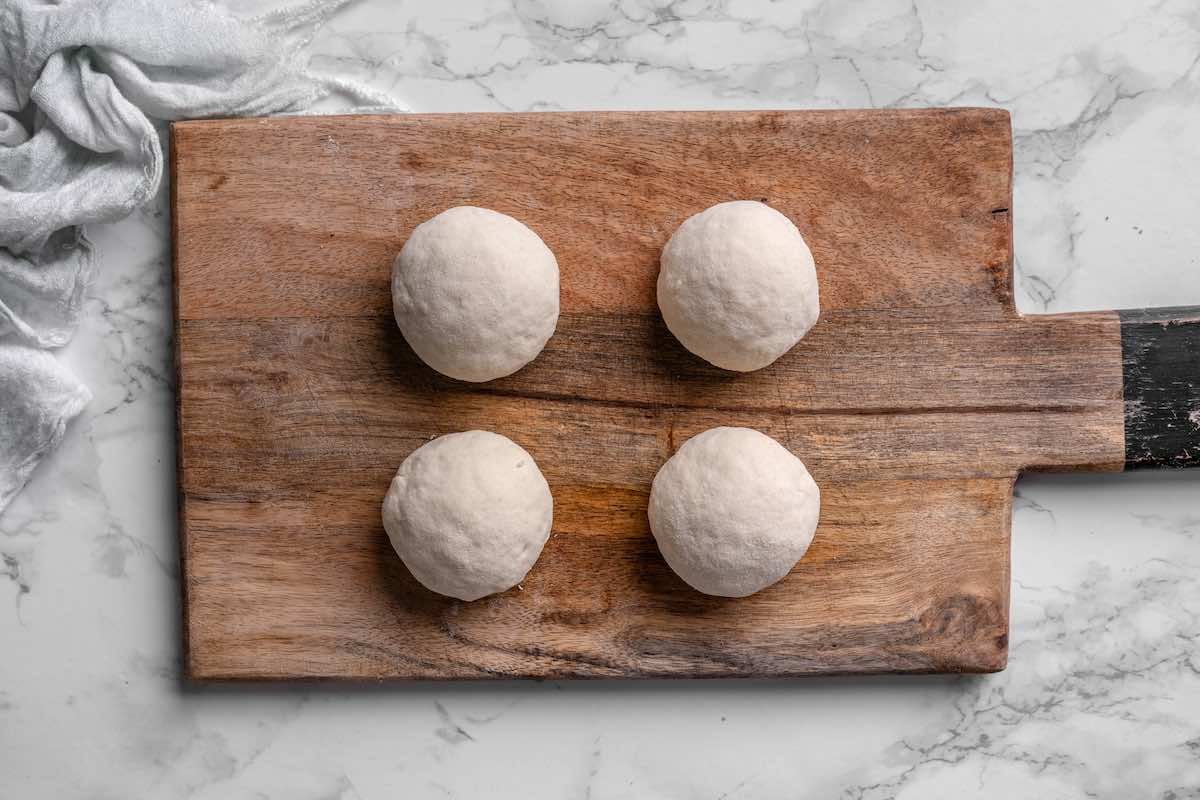 four balls of dough on a wooden board.