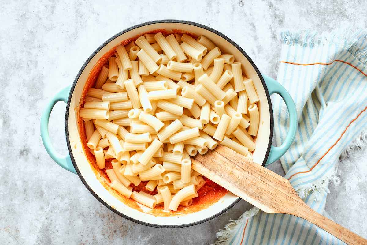 adding cooked pasta to pasta sauce.