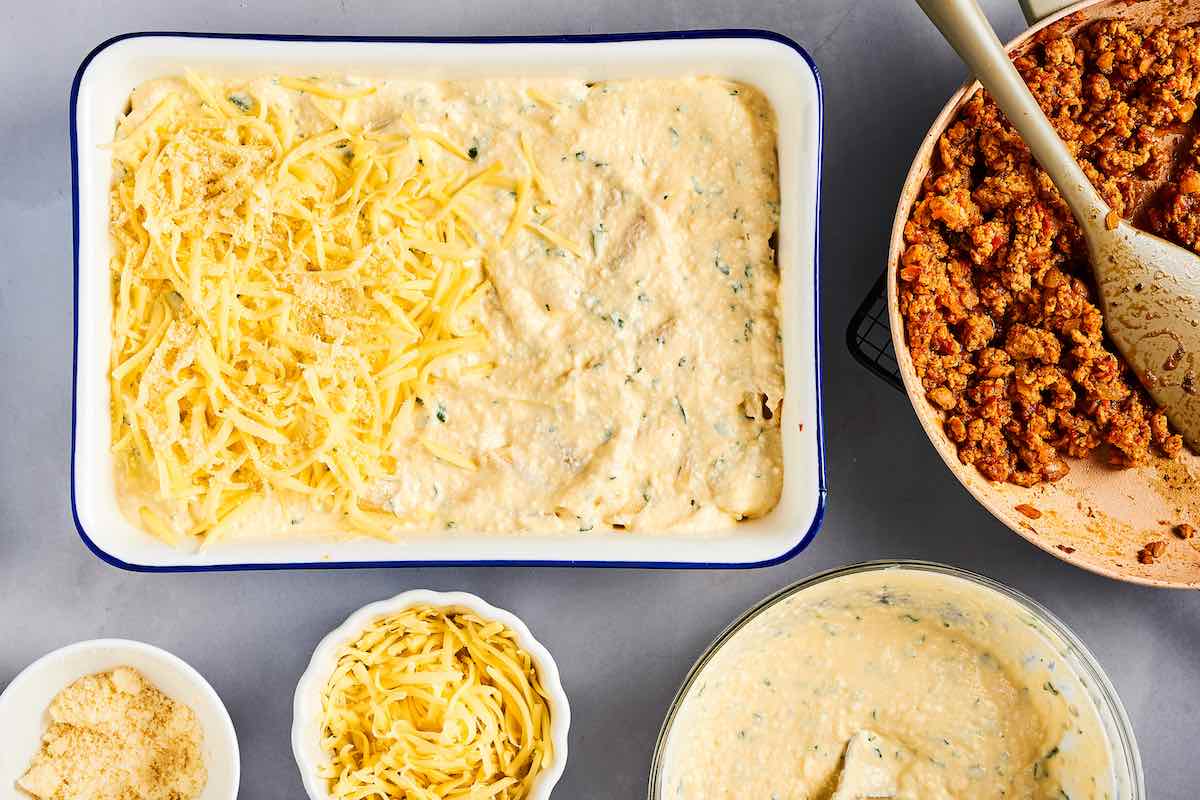 layering protein pasta with cheese sauce, shredded cheese, pasta, and meat.