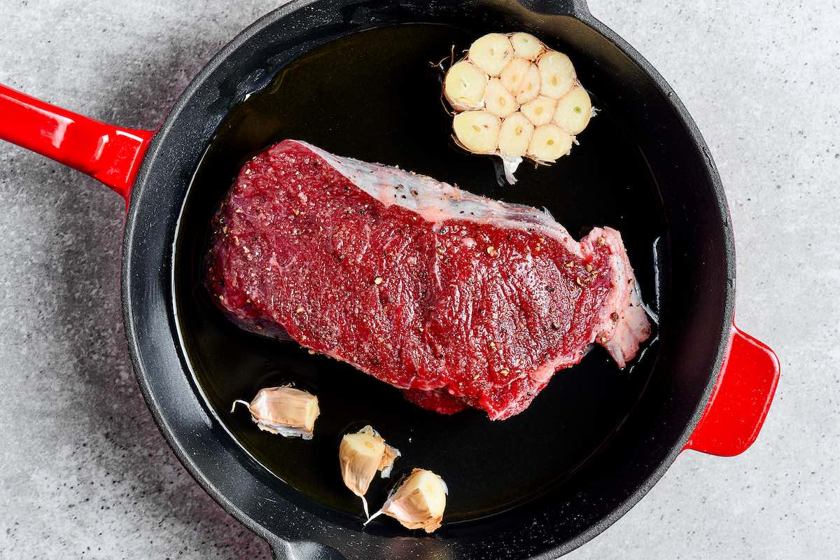 raw seasoned steak on a skillet with garlic.