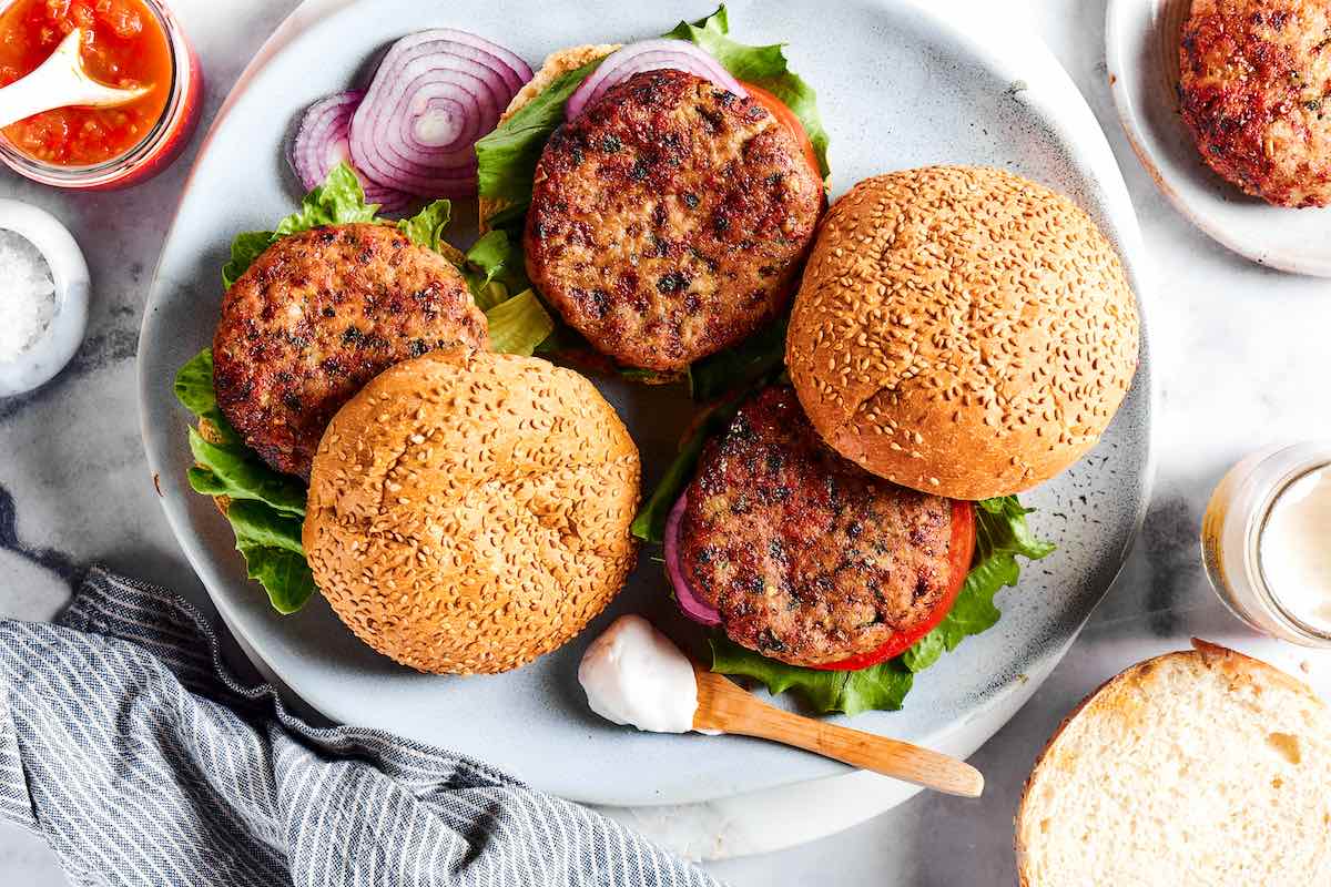 platter of cooked air fryer turkey burgers with buns, sliced onions, and tomatoes.