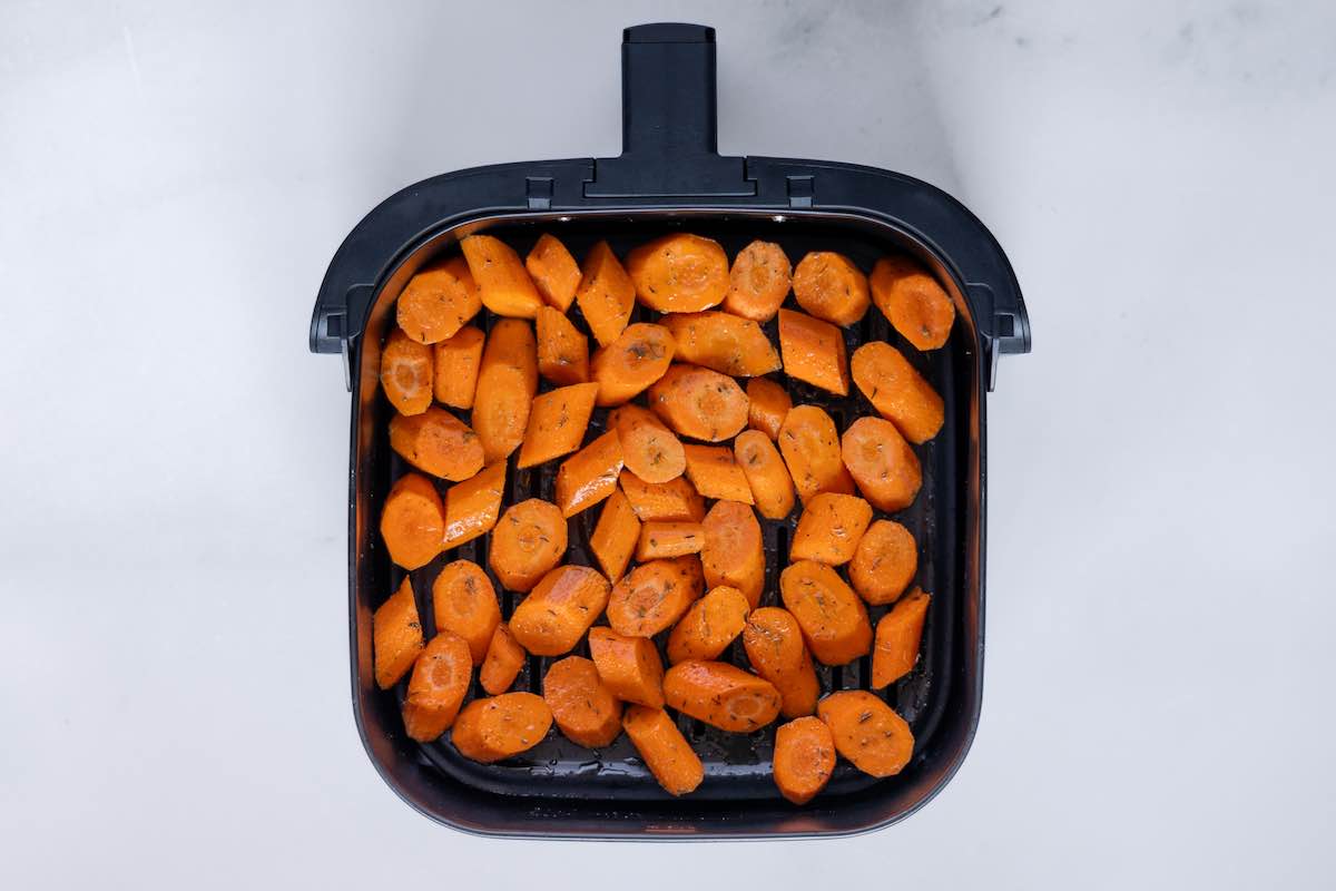 seasoned raw carrots in the air fryer basket.