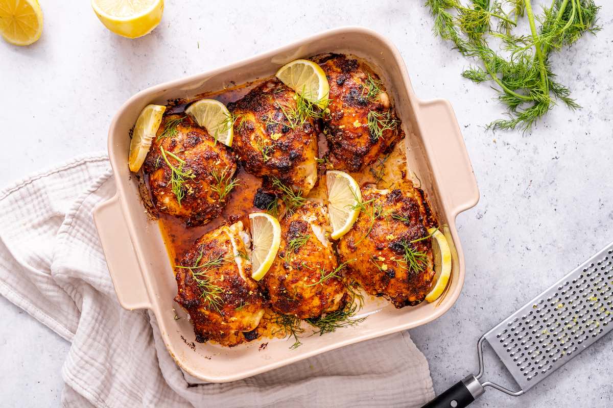 crispy baked chicken thighs in a baking dish with fresh lemon and herbs.