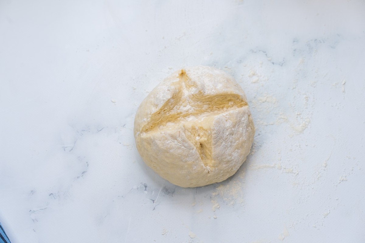 scored ball of dough on a flour surface.