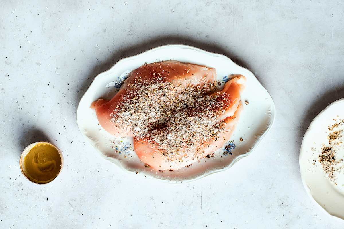 seasoned raw chicken breasts on a plate.