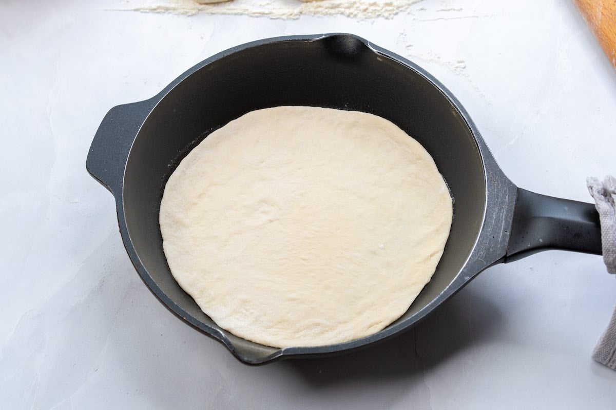 flattened raw dough in a cast iron skillet.