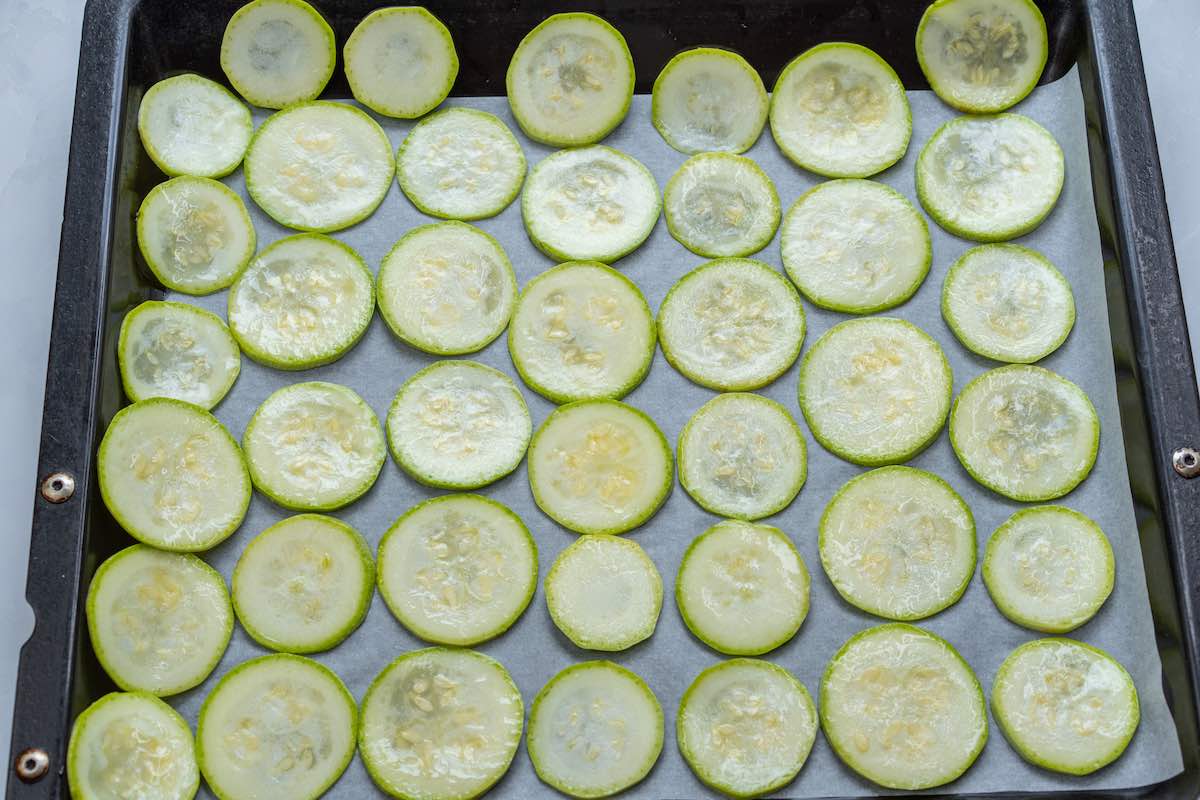 sliced and seasoned zucchini chips on a baking sheet.