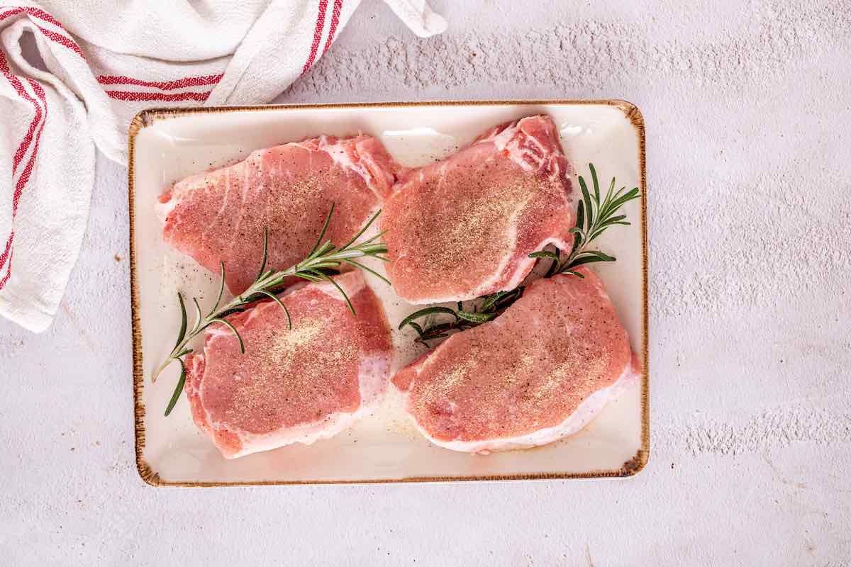 seasoned raw pork chops on a plate.