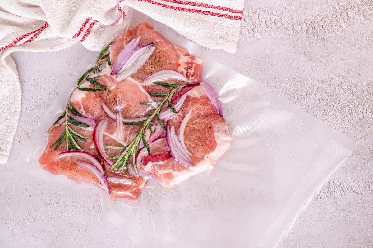 raw pork chops vacuum sealed in a bag with onions and herbs.