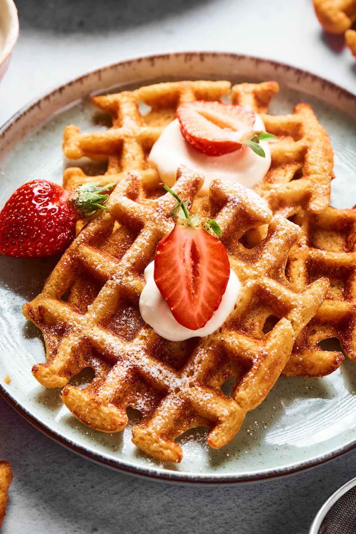 keto waffles with whipped cream and sliced strawberries on top.