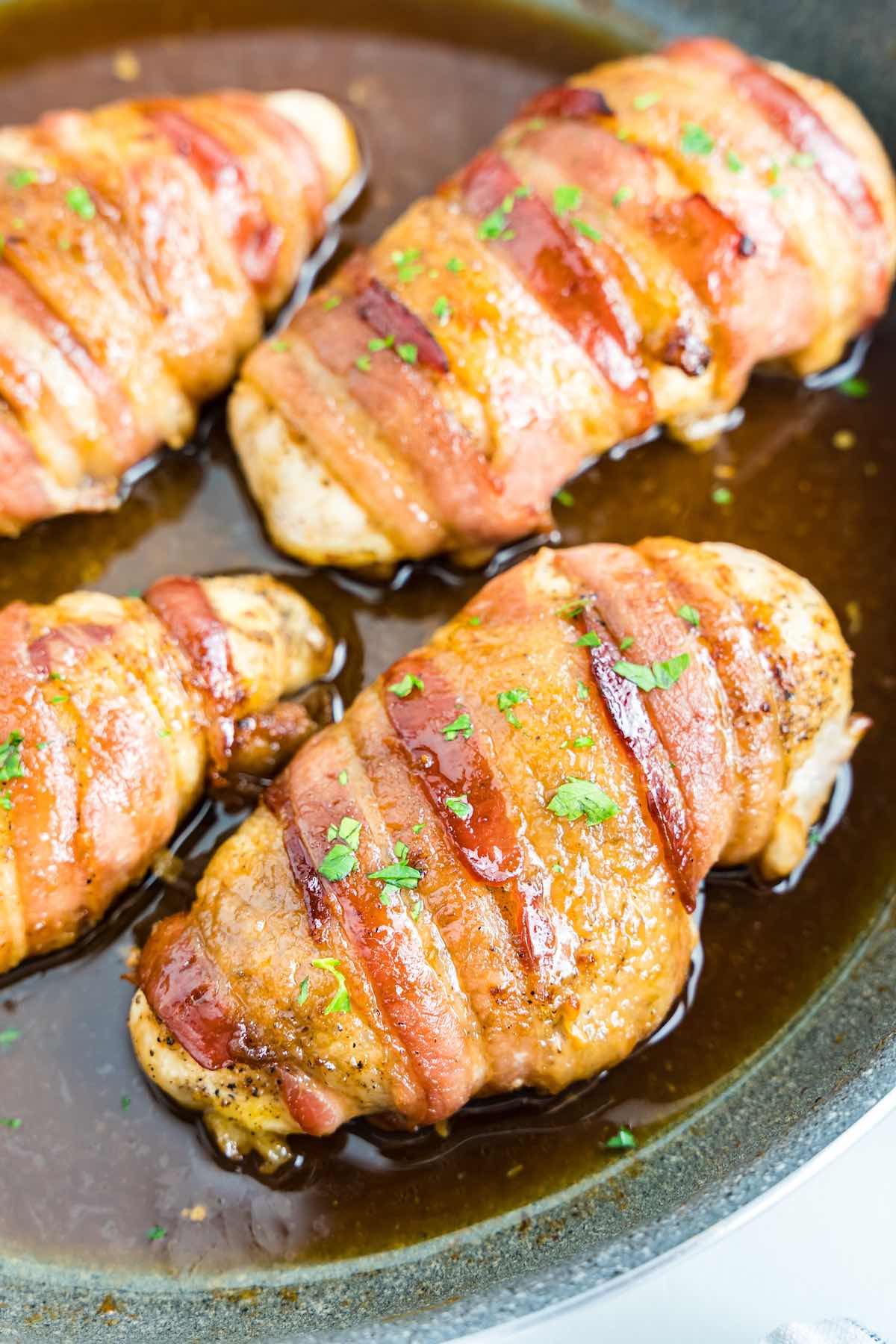 bacon wrapped chicken in a skillet with fresh parsley on top.