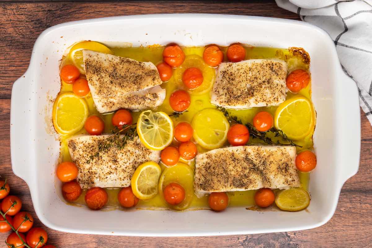 baked haddock in a baking dish with tomatoes, lemon, and olive oil.