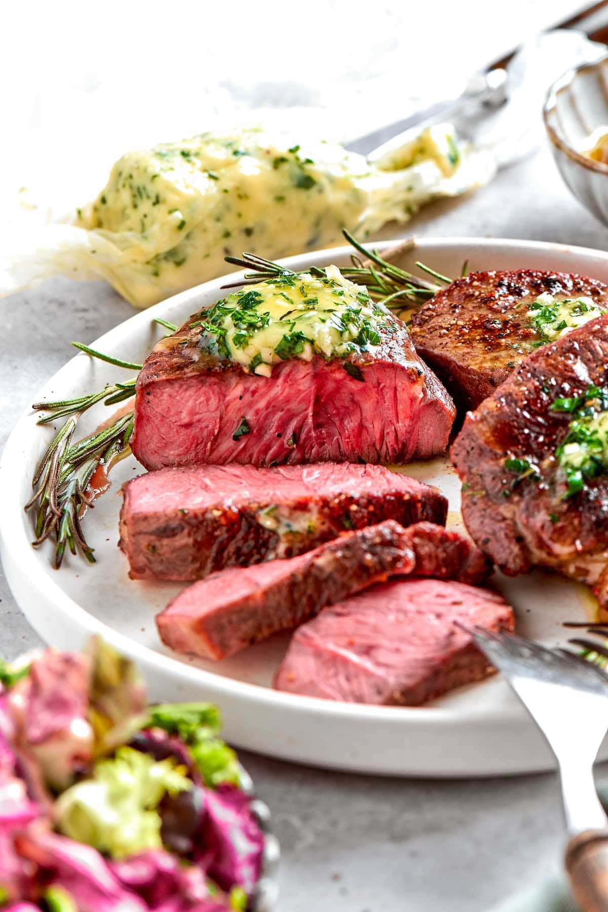 sliced filet mignon on a plate with herb butter.