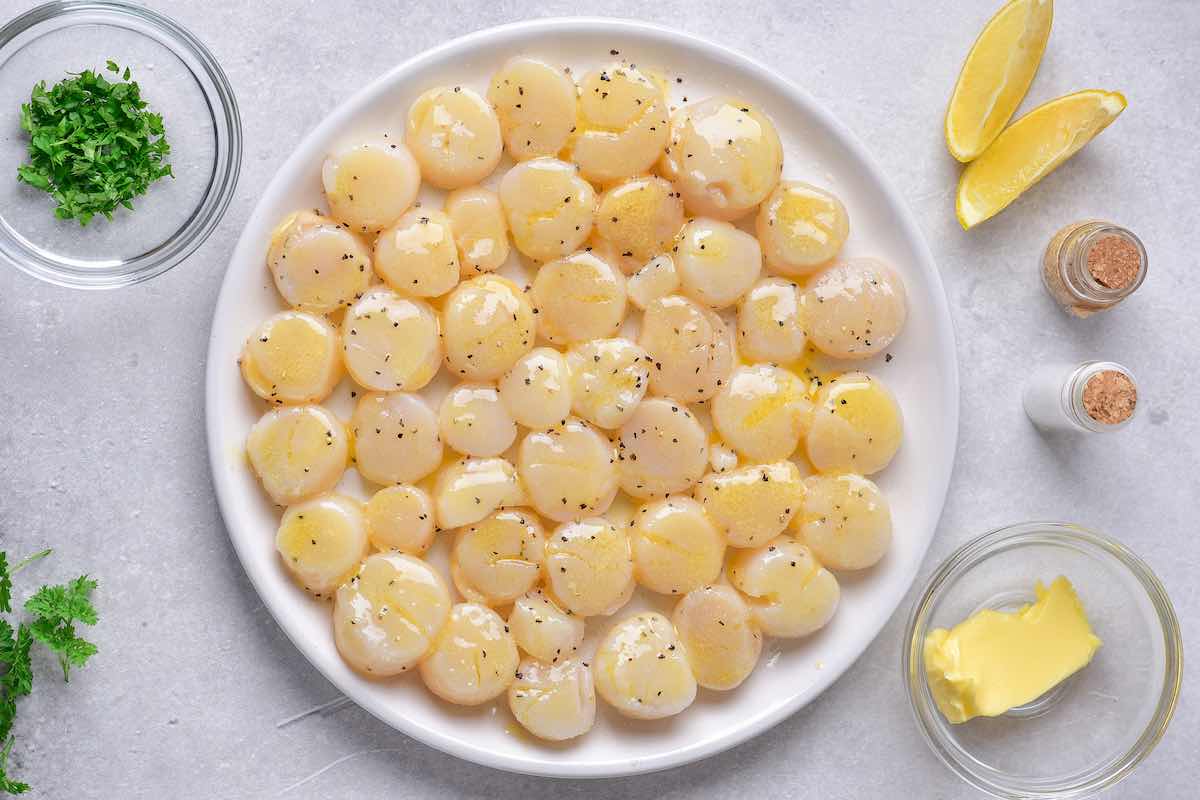 raw scallops on a plate seasoned with butter, lemon, salt, and pepper.