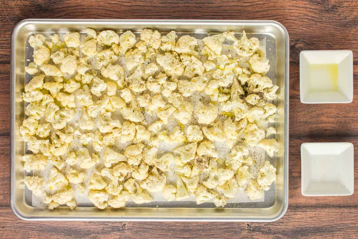 seasoned raw cauliflower florets on a roasting pan.