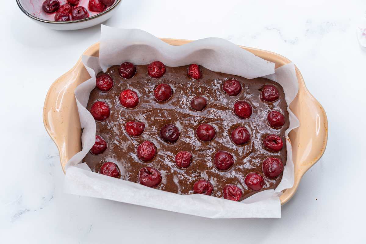 baking pan with brownie batter in it with cherries on top.