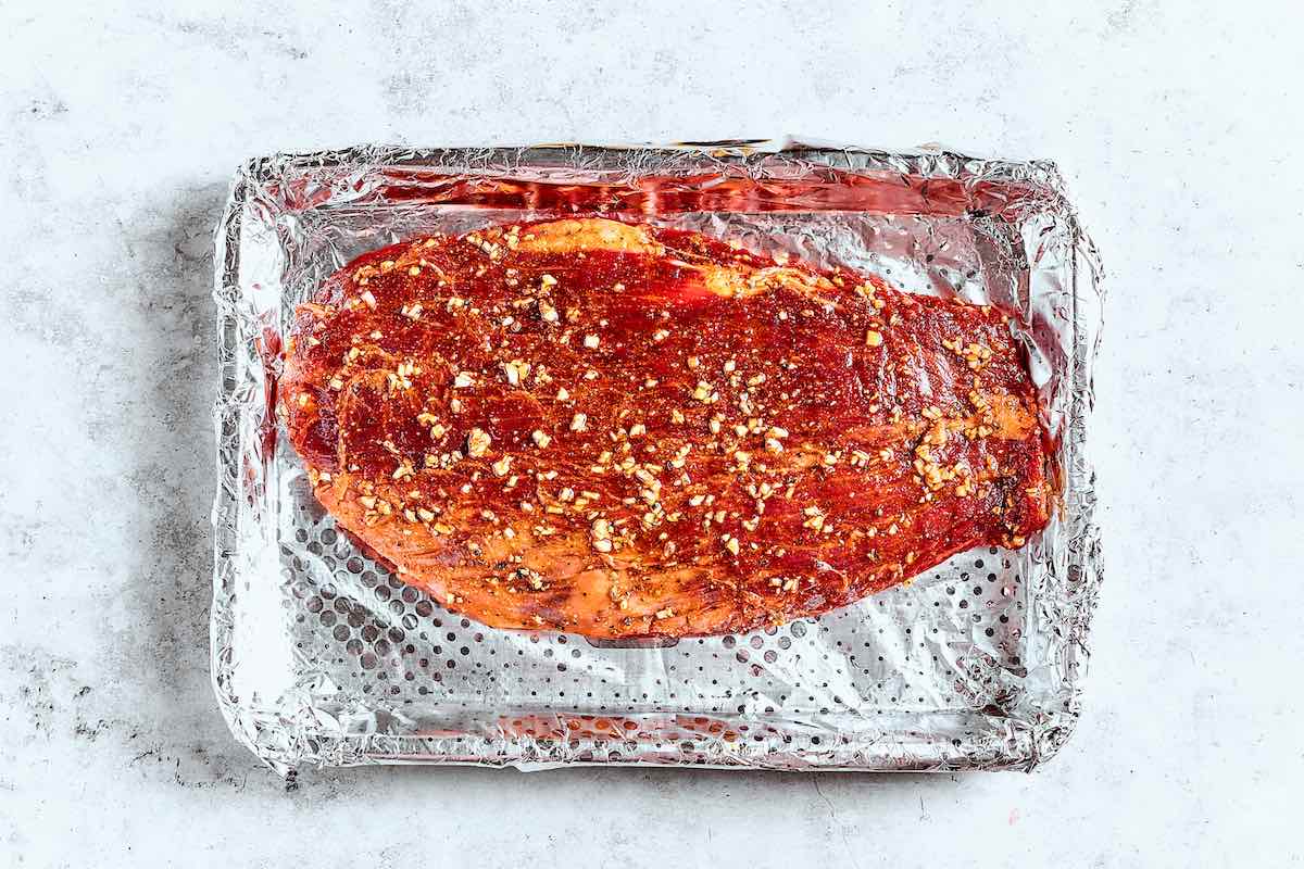 seasoned raw flat iron steak on a baking sheet.