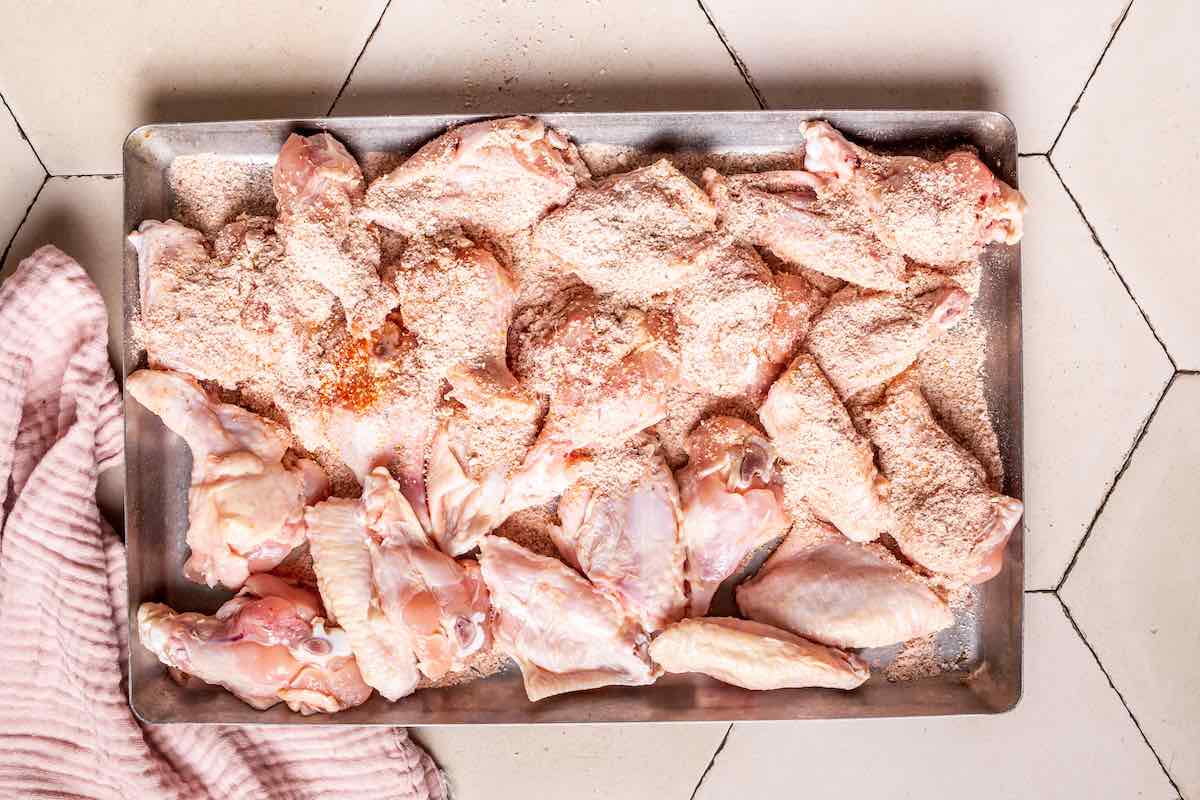 seasoning raw chicken wings on a tray.