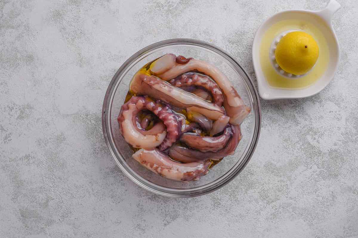 raw octopus in a bowl with olive oil and seasonings.