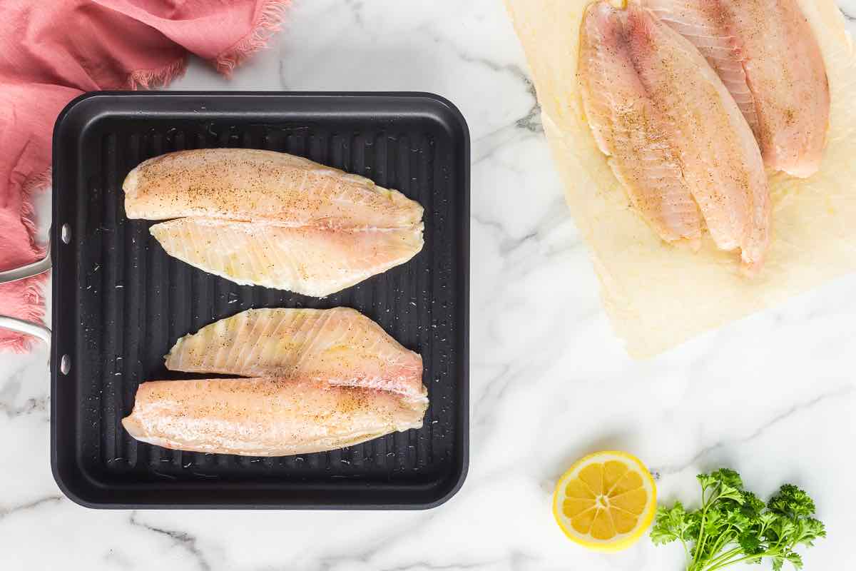 seasoned raw tilapia fillets on a grill pan.