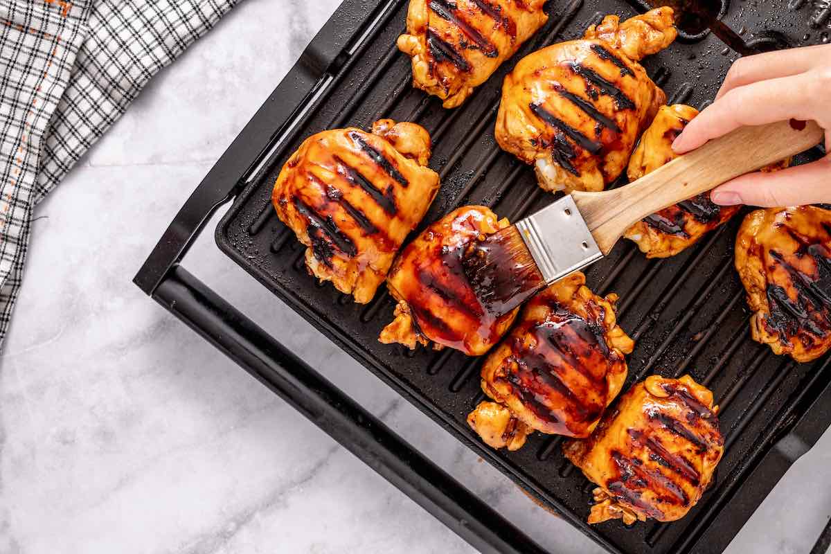 basting huli huli chicken on a grill with more sauce.