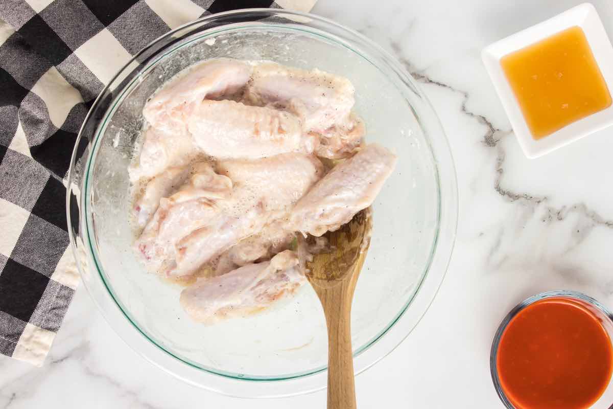 raw chicken wings in a bowl with seasonings and oil.