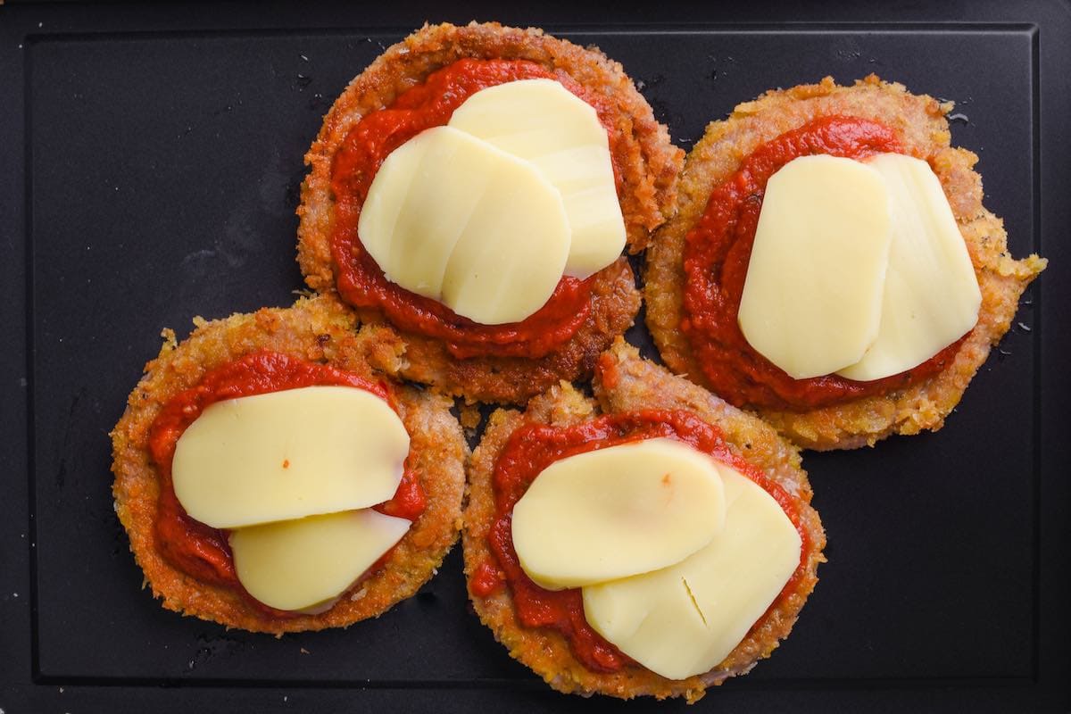 breaded veal cutlets with marinara sauce and mozzarella on baking sheet.