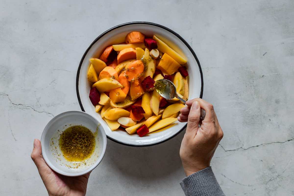 adding olive oil and seasonings to the raw vegetables in a bowl.